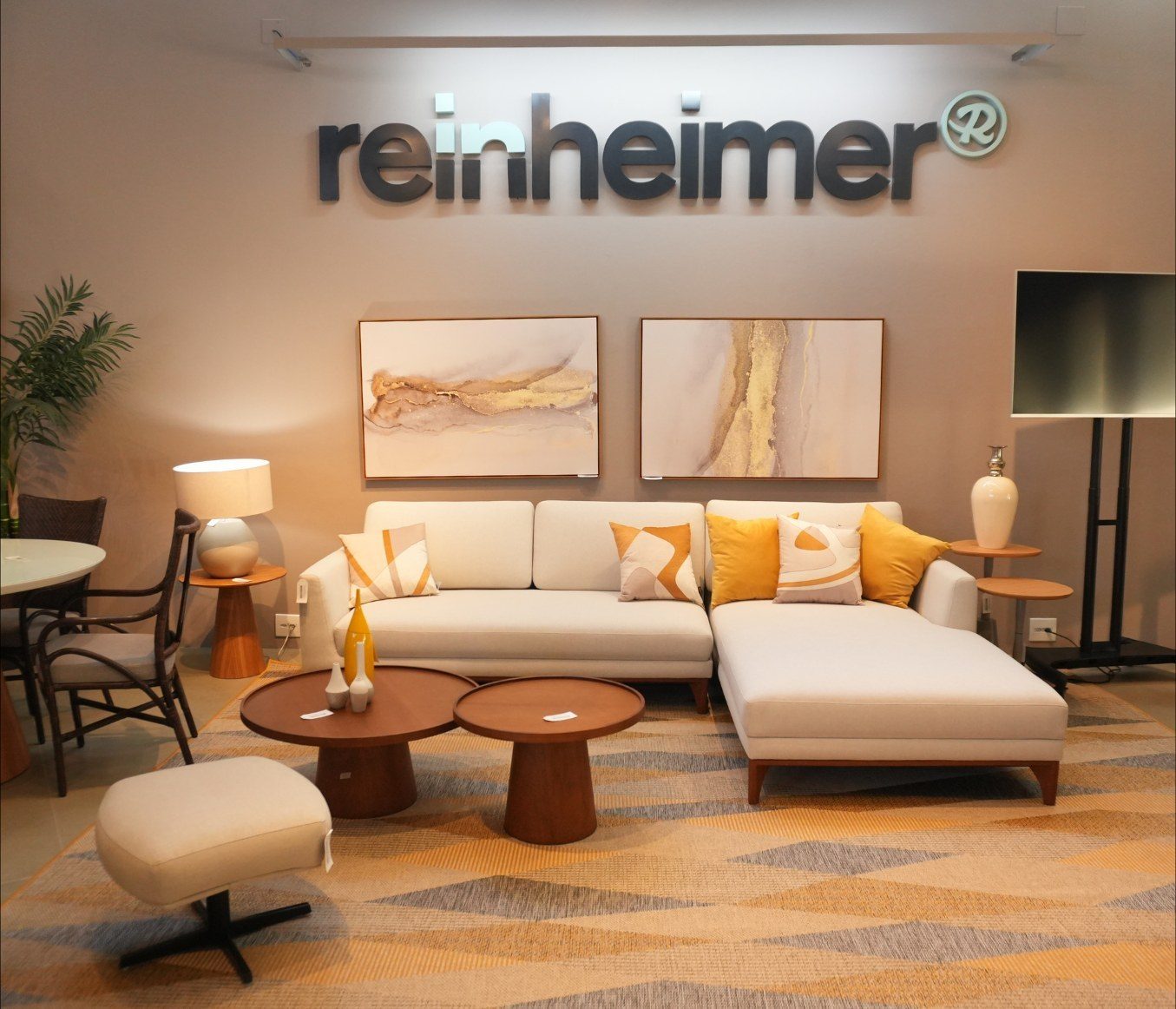 Ambiente montado no showroom da Reinheimer: sofá, tapete, mesas de centro e luminárias, sob o letreiro da loja